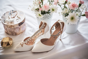 Stylish white wedding bridal shoes, perfume, flowers and jewelry.