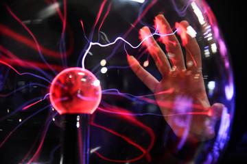 Hand touching with finger electric plasma in glass sphere.