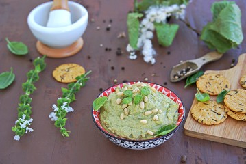 Green pea spread with almonds and basil on a brown concrete background. Decorated with pine nuts, served with crackers.