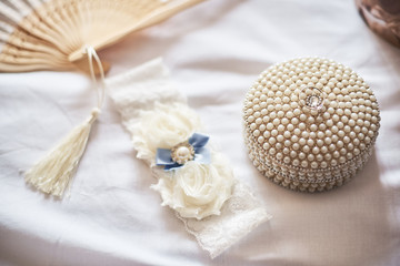 Fototapeta na wymiar Close-up of white garter and wedding ring on white background.