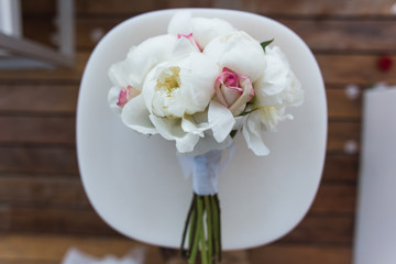 Wedding bouquet with roses and peonies lies on a white chair