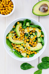 Salad from avocado, chickpea, spinach, cucumber and sesame on a white wooden table.
