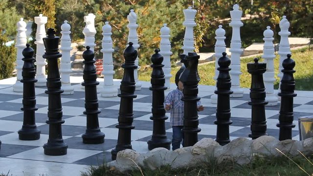 Little boy learns to play chess on big board outdoor