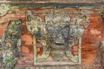 Klungkung, Bali, Indonesia - February 26, 2019: Royal Palace. Closeup of gray stone mask mural set in red brick wall.