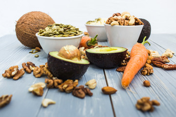 Healthy food and dieting concept. Focus on avocado and carrots. Nuts: cashews, almonds, pecans, walnuts, pumpkin seeds on a wooden table. Light summer flat lay food composition
