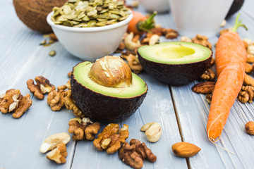 Healthy food and dieting concept. Focus on avocado and carrots. Nuts: cashews, almonds, pecans, walnuts, pumpkin seeds on a wooden table. Light summer flat lay food composition