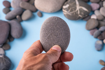 Pebble stone hold in hand on blue background with pebbles