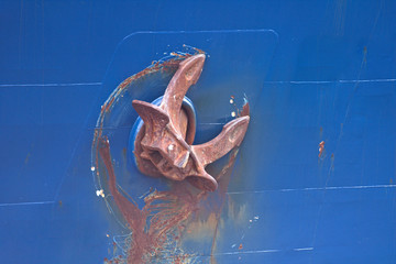 Rusty ship anchor suspended from the blue side of the ship