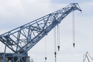 The arrow of a huge port crane with a lot of cables and hooks against the cloudy sky