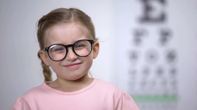 Adorable female child smiling adjusting eyeglasses, successful vision treatment