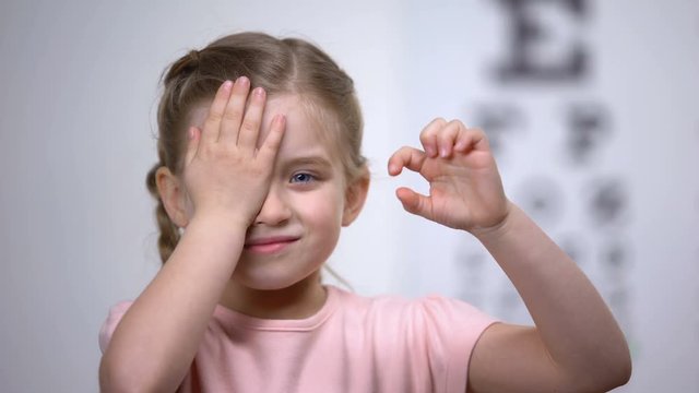 Child girl closing eye, showing size or sign from eye chart, vision diagnostics