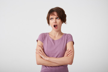 Obraz premium Portrait of frowning displeased short-haired lady in blank t-shirt, outraged by the gossip she heard from a friend, stands over white wall with arms crossed.
