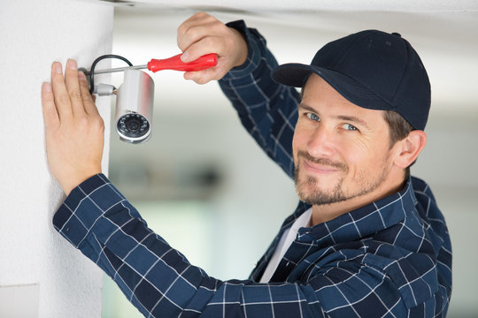 handyman fixing cctv camera to wall - Powered by Adobe