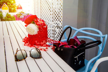 women's handbag on a chair with a white table in an open air. sun glasses and desor with flowers on the table.