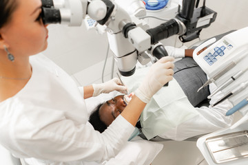 Modern equipment microscope in dental office. Young woman dentist treating root canals. Man patient lying on dentist chair with open mouth. Medicine, dentistry and health care concept.