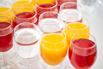 Table top full of glasses Glasses not alcoholic drinks, orange juice, water and berry juice. s with canapes and antipasti in the background.