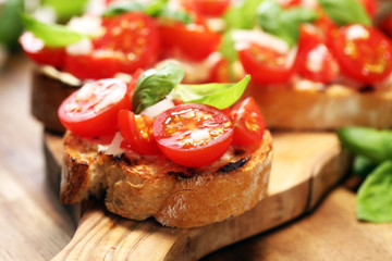Traditional italian antipasto bruschetta appetizer with cherry tomatoes, cream cheese, basil leaves and balsamic vinegar on cutting board. Antipasti