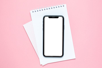 Mobile phone blank screen and business notebook on pink background.Woman working desk.