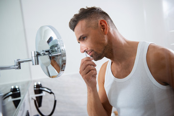 Calm man removing nose hair with tweezers