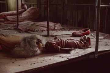 Old broken children doll toy in kindergarten, nursery school. Destroyed abandoned ghost city...