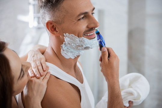 Happy man shaving his face and curious woman looking at it