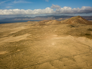 Fototapeta na wymiar Aerial view of a desert landscape on the island of Lanzarote, Canary Islands, Spain. Mountains of the village of Soo and in the background Famara. Reliefs and volcanoes on the horizon