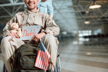 Woman carrying wheelchair and situating behind her husband in military uniform