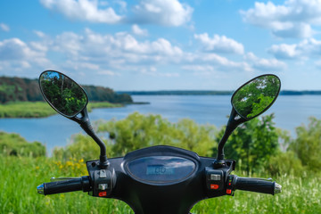 steering wheel of black electric scooter with reflection of trees in the mirrors on background of...