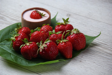 Homemade yogurt with fresh strawberry on a wooden background and few organic strawberries on a big green leaf