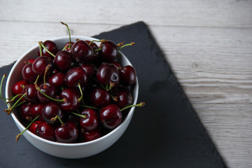 Fresh organic cherries in white plate on a wooden background.