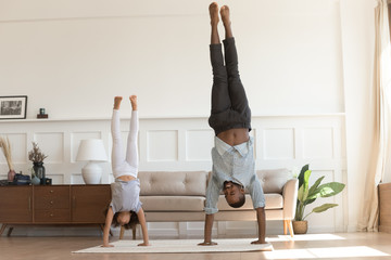 Active african kid girl copy father doing handstand at home