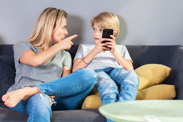 Mischievous boy looking at mother who scolding him for playing on smartphone.Childhood, technology...