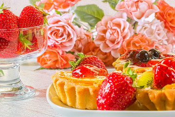 Still-life with cakes, strawberries and a bouquet of roses, close-up