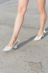 White shoes on the girl's feet. The legs in the shoes are close-up. A girl in fashionable shoes walks through the city. Asphalt underfoot. Vertical photo