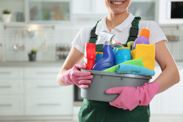 Woman with basin of detergents in kitchen, closeup. Cleaning service