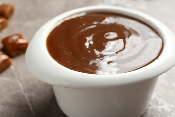 Bowl with tasty caramel sauce on table, closeup