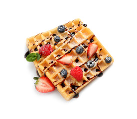 Yummy waffles with berries and chocolate syrup on white background, top view