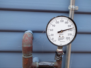 Water pressure gauge manometer with cobwebs and rusty pipes and tape outside of home. Lack of care