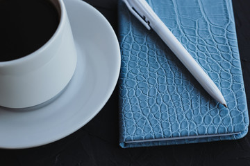 Notepad and cup of coffee on a black background.