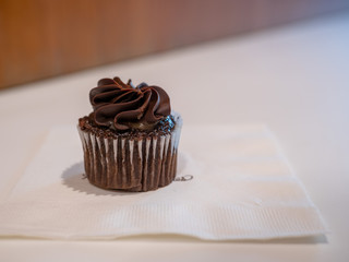 Small black chocolate cupcake sitting on napkin in on bakery table