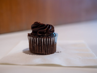 Small black chocolate cupcake sitting on napkin in on bakery table