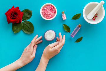 Natural floral cosmetics with rose flowers for face and body care and hands on blue background top view