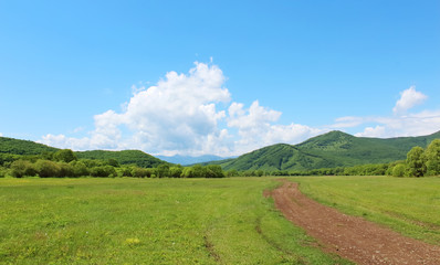Summer landscape with green grass, hills, road and clouds