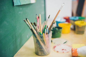 Artistic equipment in a artist studio. Paint brushes in the plastic glass. Selective focus.