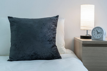 Gray cushions on the bed and lamp and alarm clock on the bedside table