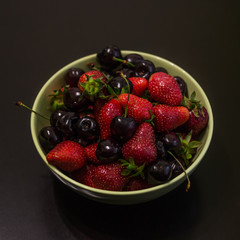 Fresh fruit of strawberries and cherries in a cup on a dark background.