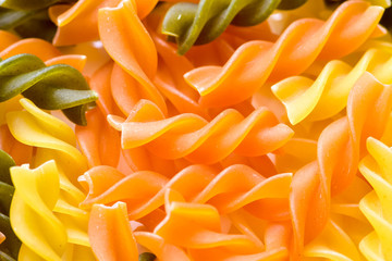 Uncooked three-colored wheat pasta with spinach and tomato, kitchen background