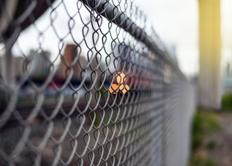 Closeup of chain link fence by railway with lights behind