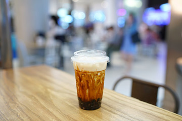 Bubble Milk Tea - A plastic glass of fresh milk with black sugar syrup (Kuromitsu) and hot black pearl (Boba) topped with cream cheese on blurred background, Taiwanese drinking culture.