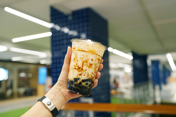 Bubble Milk Tea - Holding a plastic glass of fresh milk with black sugar syrup (Kuromitsu) and hot black pearl (Boba) on blurred background, Taiwanese style.